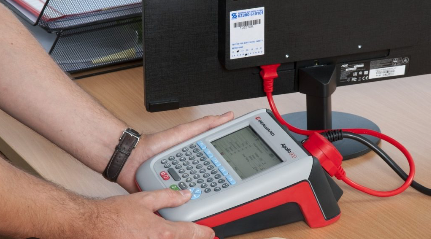 A portable appliance tester being used on an electrical device, ensuring safety compliance in the workplace.