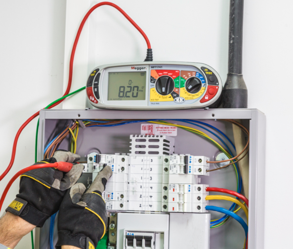 An electrician is using a multimeter to test a circuit breaker in an electrical panel. The multimeter displays a reading, and various colored wires are visible in the panel. The electrician wears gloves